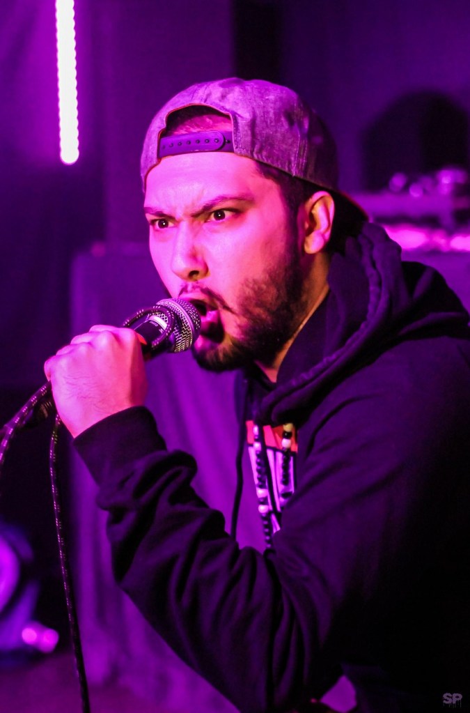 Loaneski wearing a grey baseball cap and black hoody holds the microphone close to his mouth as he delivers another heartfelt performance
