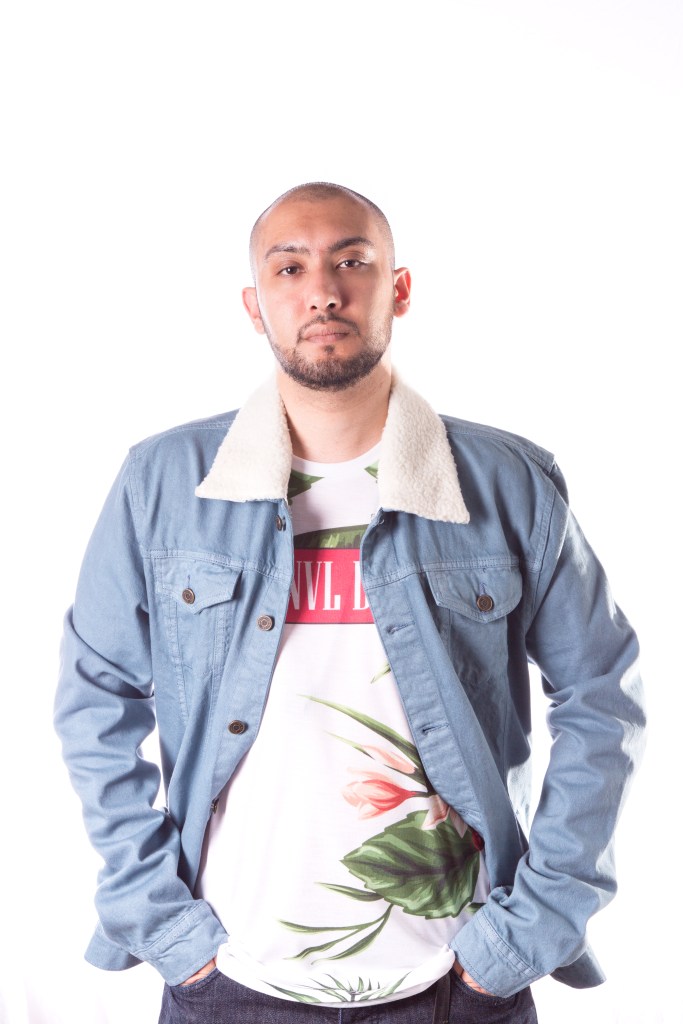 Loaneski with hands in pockets wearing a denim blue jacket with white sheep wool collar and a white tshirt with green and pink plant design