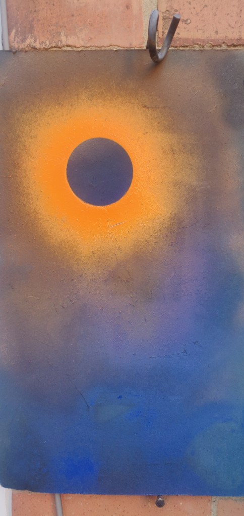 Image of acrylic spray paint on a sheet of scrap metal showing a mottled blue background with orange patch with one whole circle of orange missing 