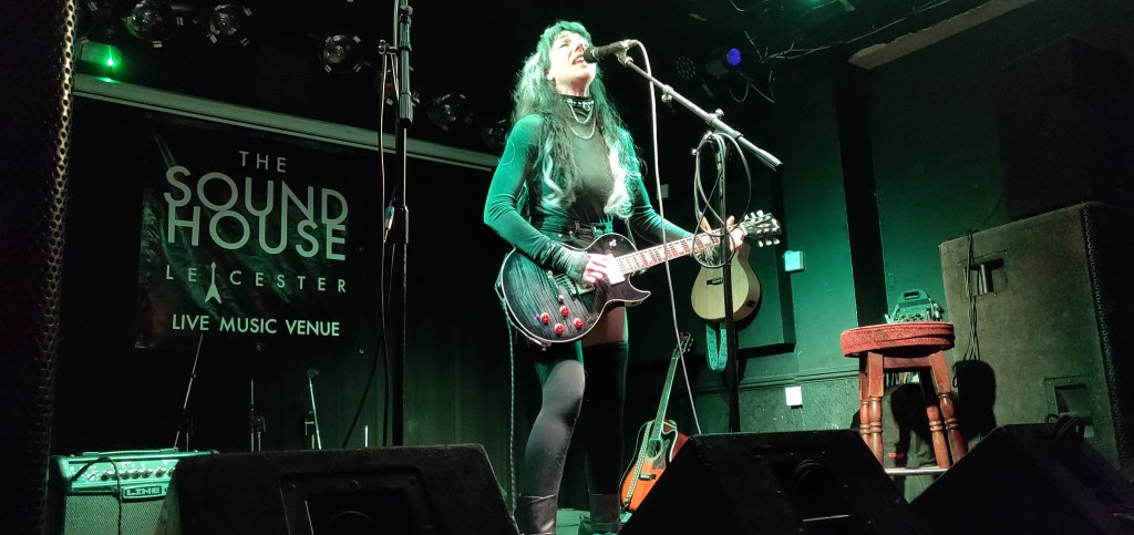 Brilliant singer songwriter Mary Singer formerly of Mia and The Moon on stage playing a guitar and singing into a microphone at the Sound House in Leicester